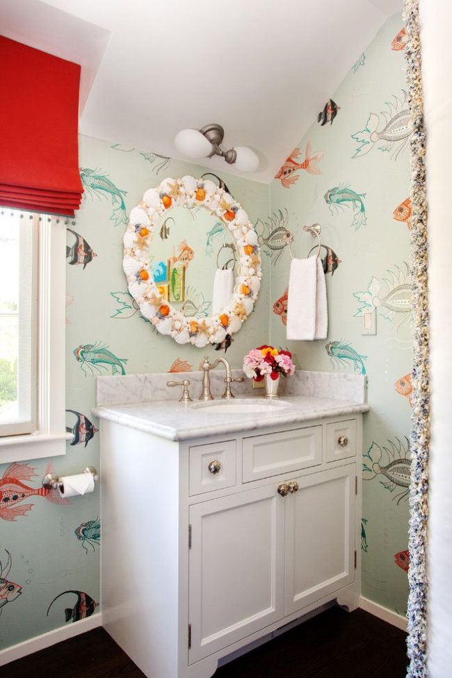 Salle de bain avec un thème marin et un papier peint pastel doux avec des images graphiques de différents types de poissons.  Miroir coquillage fait à la main - une caractéristique de l'intérieur