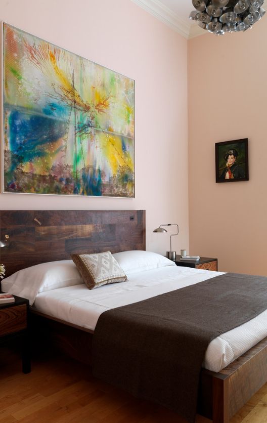 Le tableau à l'abstraction lumineuse se combine harmonieusement avec une tête de lit en bois et un mur de couleur pastel