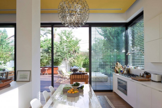 Stores inhabituels dans une cuisine de studio aux couleurs claires avec des accents sur les éléments intérieurs en bois et un plafond jaune vif dans une maison privée
